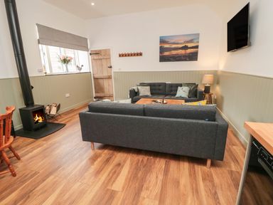 A living room with two sofas a wood stove and a wall mounted television at The Bakery in Middleton near Belford