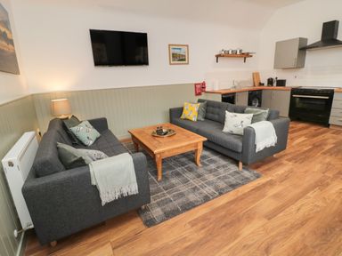 A living area with two gray sofas and a wooden coffee table next to a kitchen with gray cabinets and black appliances at The Bakery in Middleton near Belford