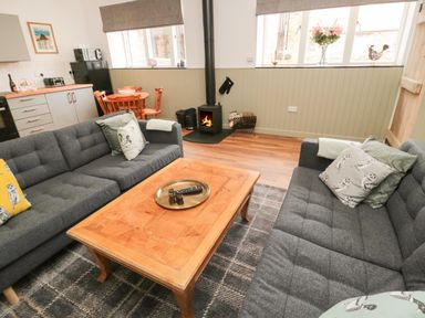 A living room with gray sofas, a wooden coffee table, and a wood-burning stove at The Bakery in Middleton near Belford