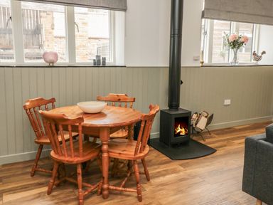 A dining area with a round wooden table and four chairs next to a wood burning stove with fire at The Bakery in Middleton near Belford