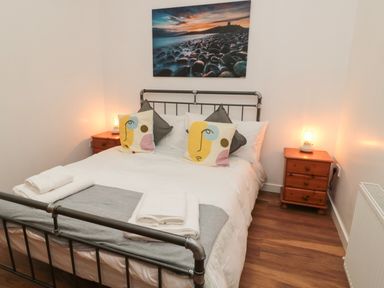 A bedroom with a metal bed frame wooden bedside tables with lamps and abstract face cushions at The Bakery in Middleton near Belford