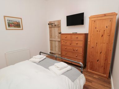 A bedroom with a bed folded towels on it a wooden wardrobe chest of drawers and a wall mounted television at The Bakery in Middleton near Belford