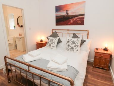 A bedroom with a metal bed frame bedside tables and a bathroom visible through an open door at The Bakery in Middleton near Belford