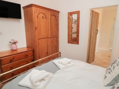 A bedroom with a wooden wardrobe dresser a wall mirror a bed with towels and a door leading to a bathroom at The Bakery in Middleton near Belford