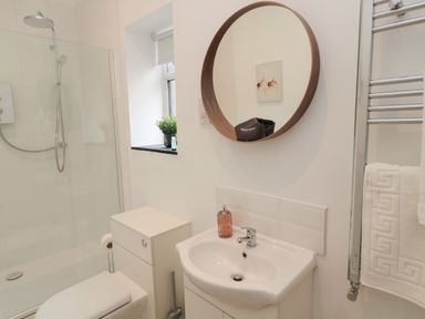 A bathroom with a toilet sink shower and round mirror at The Bakery in Middleton near Belford