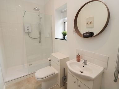A bathroom with a shower, toilet, sink, round mirror and small window at The Bakery in Middleton near Belford