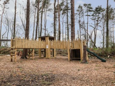 A wooden playground structure with a slide in a forest clearing at The Bakery in Middleton near Belford
