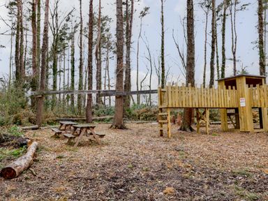 A wooded outdoor area with wooden picnic tables and a playground structure at The Bakery in Middleton near Belford