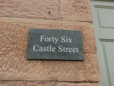 A stone wall with a sign showing Forty Six Castle Street at 46 Castle Street in Norham