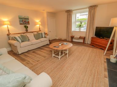 A living room with two sofas a round wooden coffee table a television on a wooden stand a small bench under a window and table lamps at 46 Castle Street in Norham