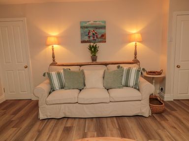 A beige sofa with cushions and a plant on a shelf with two lit lamps on the sides at 46 Castle Street in Norham