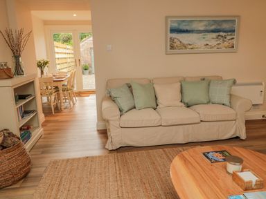 A living room with a beige sofa and cushions next to a wooden coffee table and a dining area with a table and chairs at 46 Castle Street in Norham
