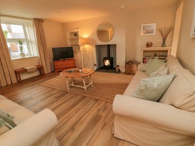A living room with a wood stove a round wooden coffee table and two sofas at 46 Castle Street in Norham