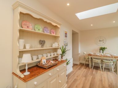 A dining area with a wooden hutch holding plates and mugs and a dining table with chairs set for a meal at 46 Castle Street in Norham