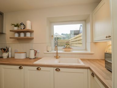 A kitchen with a sink and faucet under a window with a pitcher on the windowsill and shelves with canisters and a plant at 46 Castle Street Norham