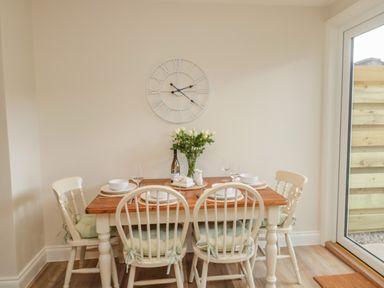A dining area with a wooden table set for four with white chairs and a wall clock at 46 Castle Street in Norham