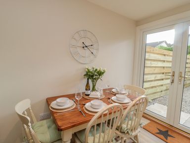 A dining area with a wooden table set for four with bowls glasses and cutlery and white chairs next to glass doors at 46 Castle Street in Norham