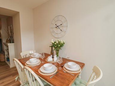 A dining table set for four with white plates and bowls a vase of white flowers and a wall clock at 46 Castle Street in Norham