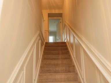 A carpeted staircase with white paneled walls and an open door at the top at 46 Castle Street in Norham