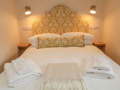 A bed with patterned headboard and cushions with folded towels and a blanket at 46 Castle Street in Norham