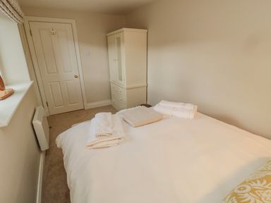 A bedroom with a bed, folded towels on the bed, a white wardrobe, and a door at 46 Castle Street Norham