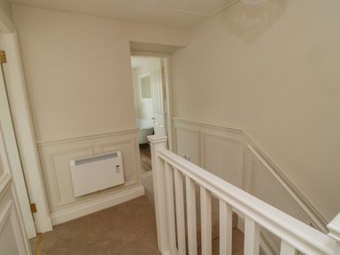 A stairway landing with a white radiator and a view into a bathroom with a bathtub at 46 Castle Street in Norham