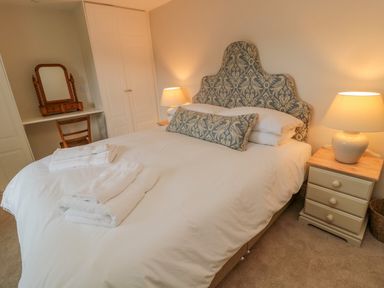 A bedroom with a bed with patterned headboard white bedding and towels bedside tables with lamps and a dressing table with a mirror and chair at 46 Castle Street in Norham