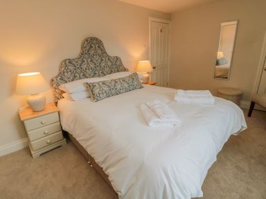 A bedroom with a patterned headboard a bed with white linens two bedside tables with lamps a mirror on the wall and folded towels on the bed at 46 Castle Street in Norham