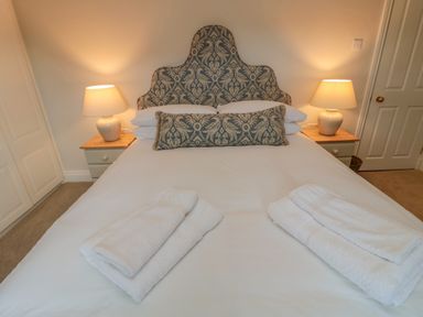 A bedroom with a double bed with patterned headboard and cushions two bedside tables with lamps and folded towels on the bed at 46 Castle Street in Norham