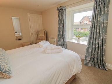 A bedroom with a bed white linens towels on bed an armchair window with patterned curtains and a plant on sill at 46 Castle Street Norham