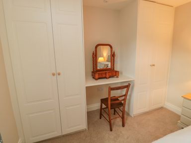 A bedroom corner with white built-in wardrobes a wooden chair and a wooden dressing table mirror at 46 Castle Street Norham