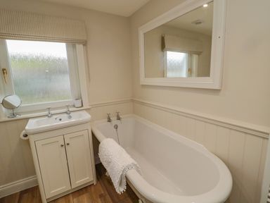 A bathroom with a bathtub a sink under a window and a large mirror above the bathtub at 46 Castle Street in Norham