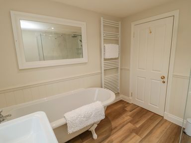A bathroom with a bathtub a wall mirror a towel warmer and a door at 46 Castle Street in Norham