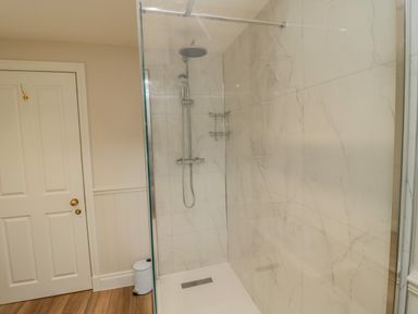 A shower area with glass door white tiles and silver fixtures next to a white door and small trash bin at 46 Castle Street in Norham