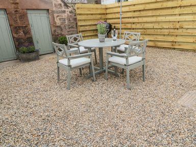 An outdoor seating area with four chairs and a round table on gravel at 46 Castle Street Norham