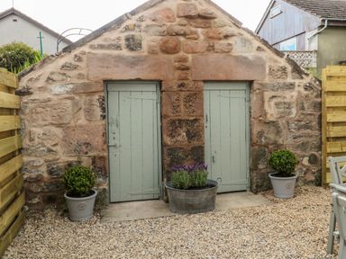 A stone wall with two light green doors and potted plants on a gravel ground at 46 Castle Street in Norham