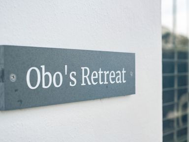 A close up of a sign reading Obos Retreat on a white wall at Obo's Retreat in St Minver near Rock