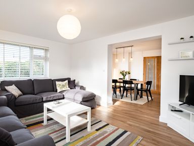 A living room with dark gray sofas a white coffee table a striped rug and a view of a dining area at Obos Retreat in St Minver near Rock