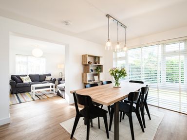 A dining area with a wooden table and six black chairs next to large windows with blinds at Obo's Retreat in St Minver near Rock