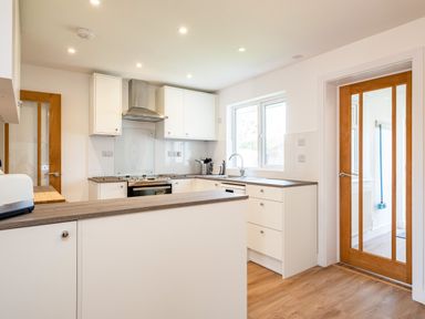 A kitchen with white cabinets wooden countertops stainless steel stove and two wooden door panels at Obos Retreat in St Minver near Rock