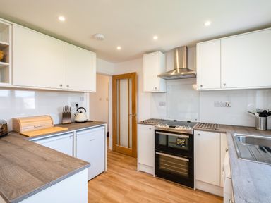 A kitchen with white cabinets a stove a kettle and a wooden cutting board at Obos Retreat in St Minver near Rock