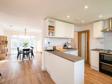 A kitchen with stove toaster and kettles next to a dining area with table chairs and shelves at Obos Retreat in St Minver near Rock