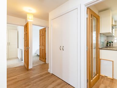 A hallway with wooden floor and multiple wooden and white doors leading to bedrooms and kitchen at Obos Retreat in St Minver near Rock