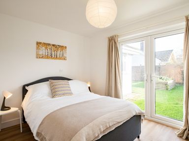 A bedroom with a bed a bedside table lamps a window with curtains and a view of a garden at Obos Retreat in St Minver near Rock
