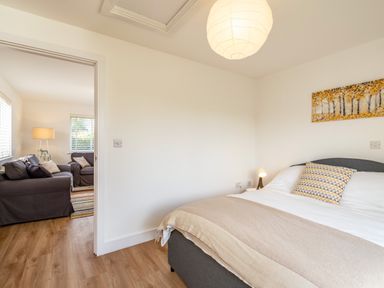 A bedroom with a bed and pillow next to a living room with sofas and a lamp at Obo's Retreat in St Minver near Rock
