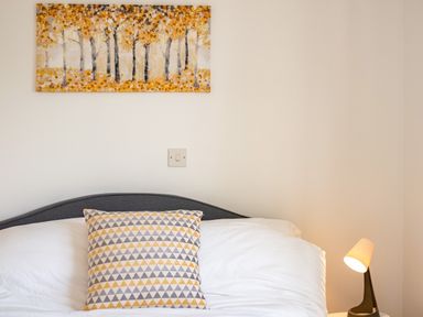 A bed with a patterned pillow a painting of trees above and a bedside lamp at Obos Retreat in St Minver near Rock