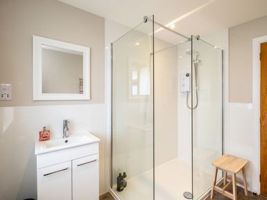 A bathroom with a shower enclosure a sink with cabinet and a wooden stool at Obos Retreat in St Minver near Rock