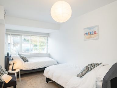 A bedroom with two single beds a window with blinds two lamps a chair and a painting on the wall at Obos Retreat in St Minver near Rock