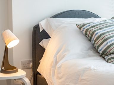 A bedside table with a lamp next to a bed with white bedding and a striped pillow at Obos Retreat in St Minver near Rock