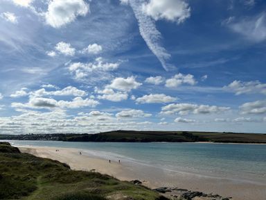 A beach with people walking along the sandy shore and grassy dunes by the water at Obos Retreat in St Minver near Rock